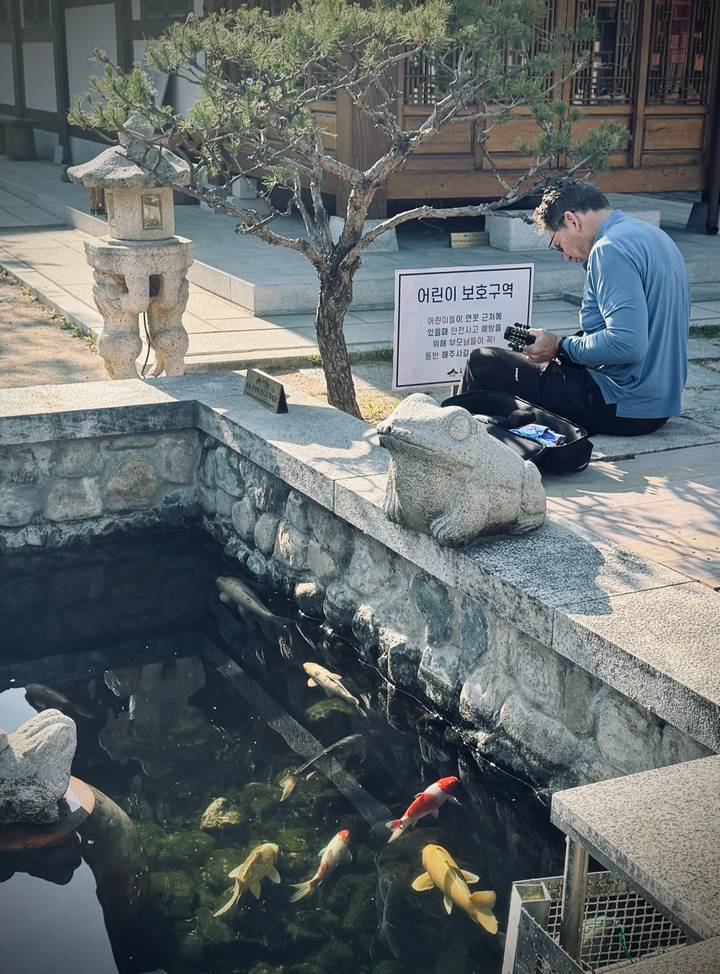 Man resting near small koi pond with stone frog statue and bilingual sign