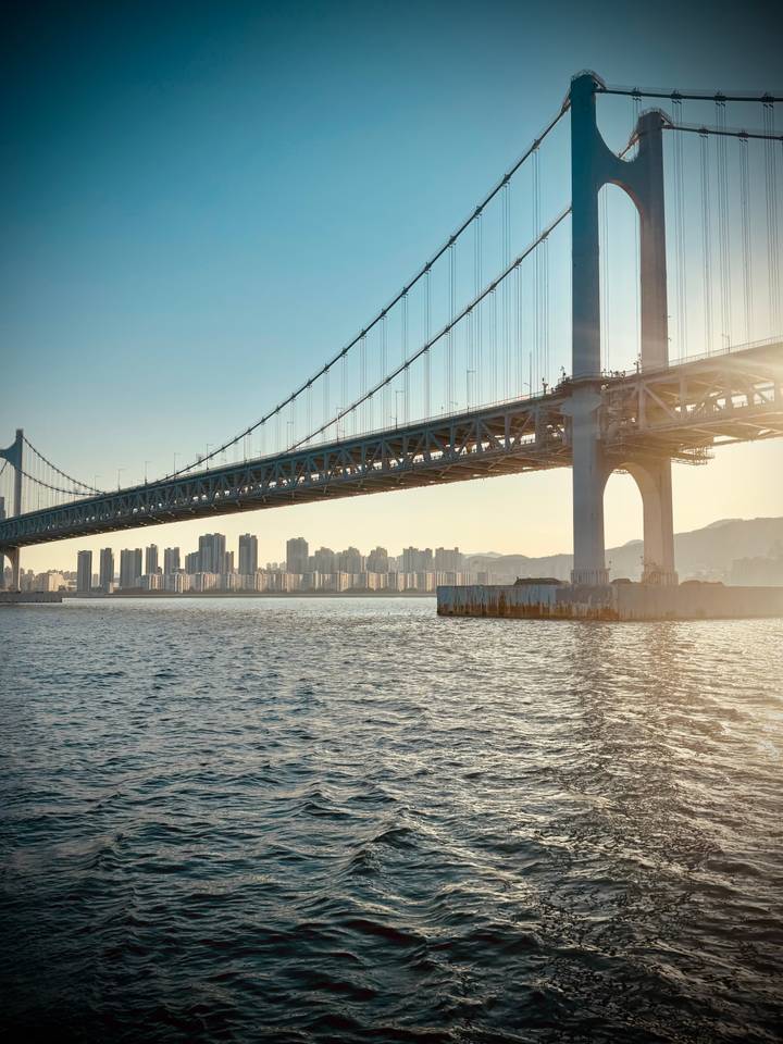 Gwangan suspension bridge stretching over water at golden hour with Busan skyline beyond