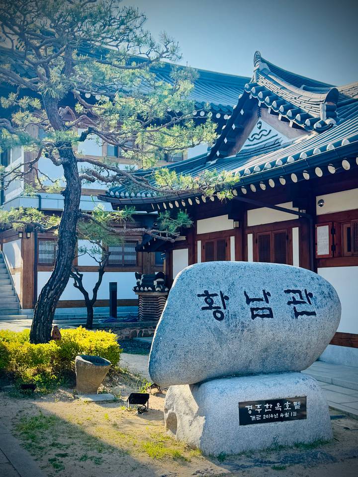 Traditional Korean building with pine tree and engraved boulder in foreground