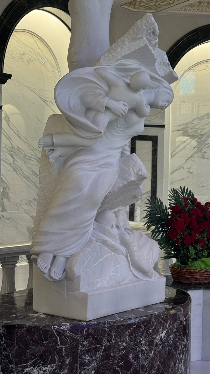 Indoor white marble sculpture of angelic figure with bouquet of red roses beside