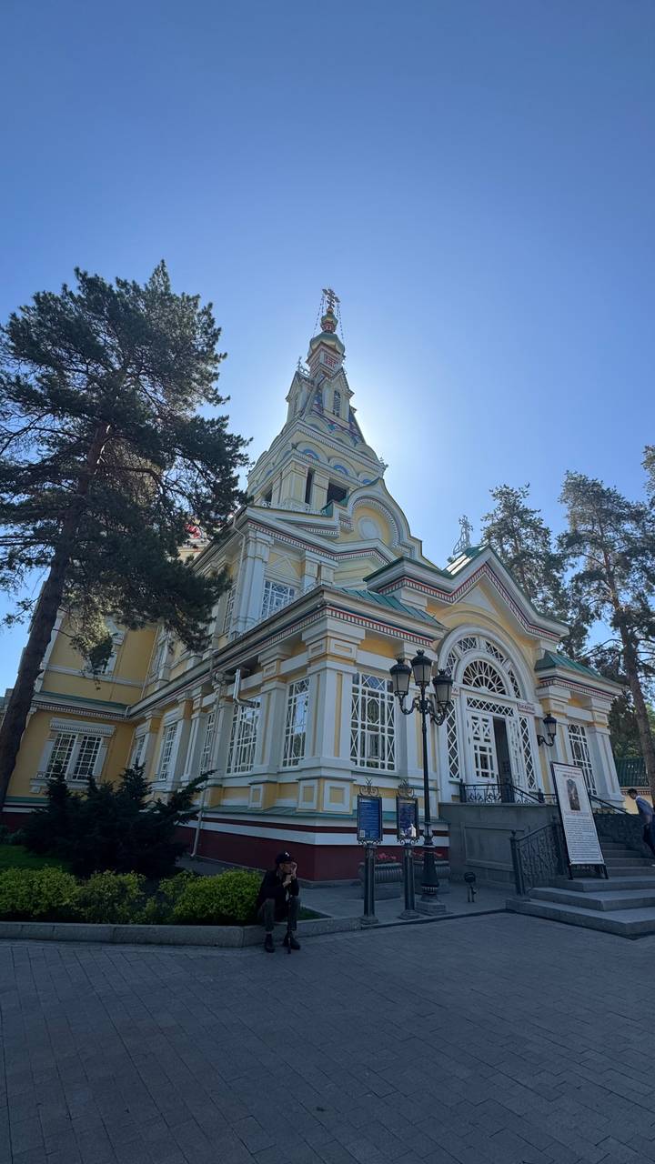 Brightly painted wooden cathedral with white trim framed by tall pine trees under a clear blue sky.