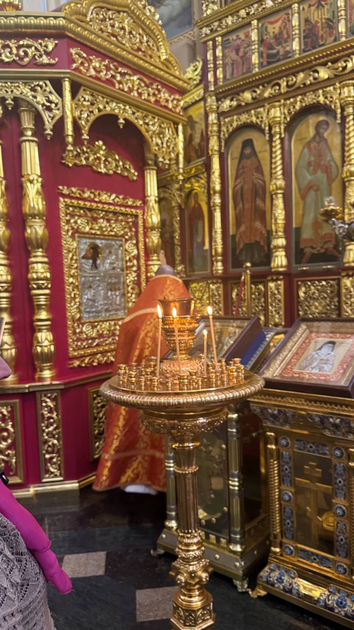 Close-up of lit prayer candles in an ornate gold stand before richly decorated icons.