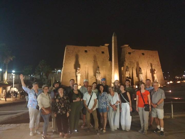 Tour group poses at night before the illuminated statues and pylon of Luxor Temple.