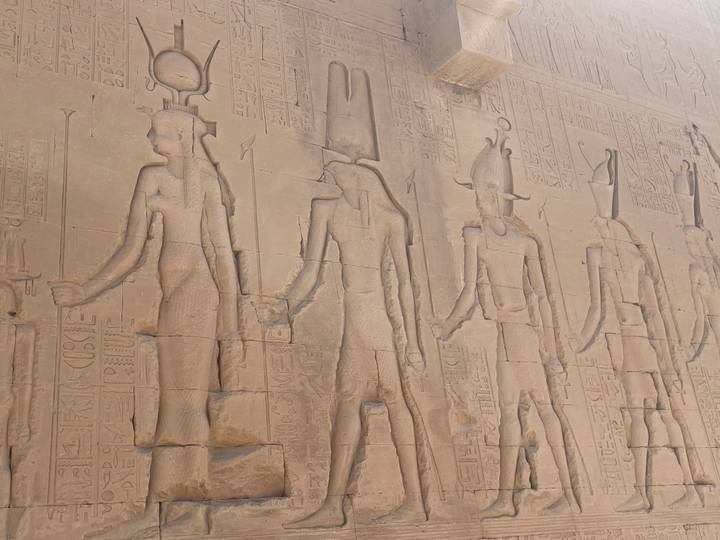 Detailed hieroglyphic and relief carvings of pharaohs and deities on a sandstone temple wall.