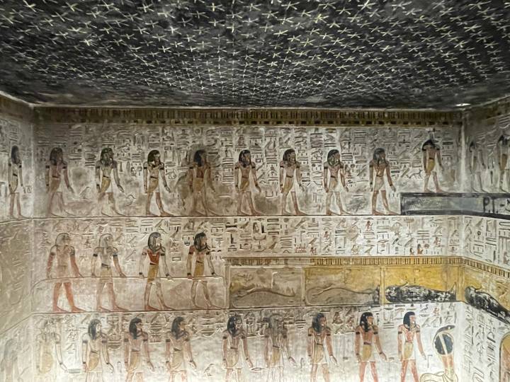Interior tomb chamber richly painted with rows of Egyptian figures and starry ceiling detail.