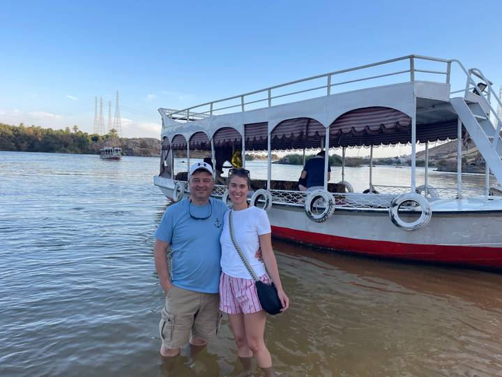 Smiling couple poses beside a small covered boat on the calm Nile River.