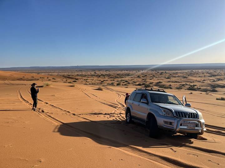 4x4 vehicle parked on vast golden dunes while a traveller photographs the desert landscape