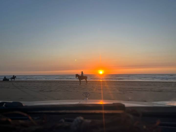Silhouette of a horseback rider on a wide beach at vibrant sunset with the sun touching the horizon