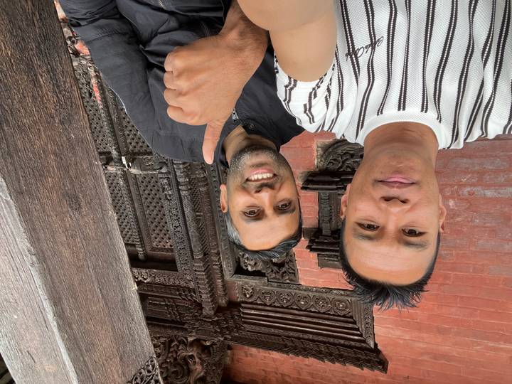 Two men smiling in front of intricately carved brick and wooden temple architecture.