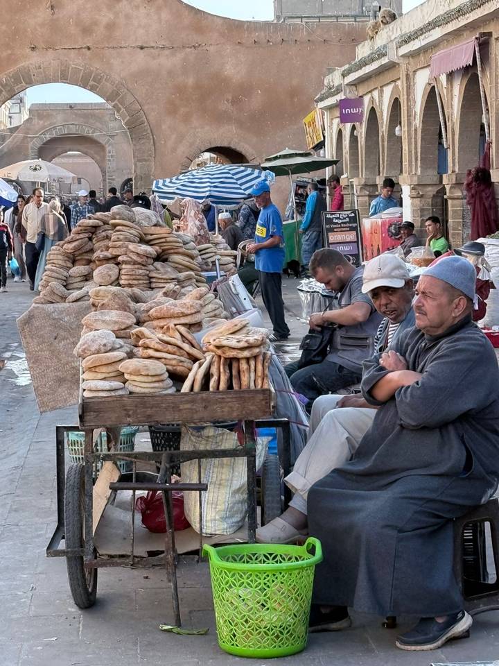 Men sit by stacked rounds of fresh flatbread at a traditional street market stall.