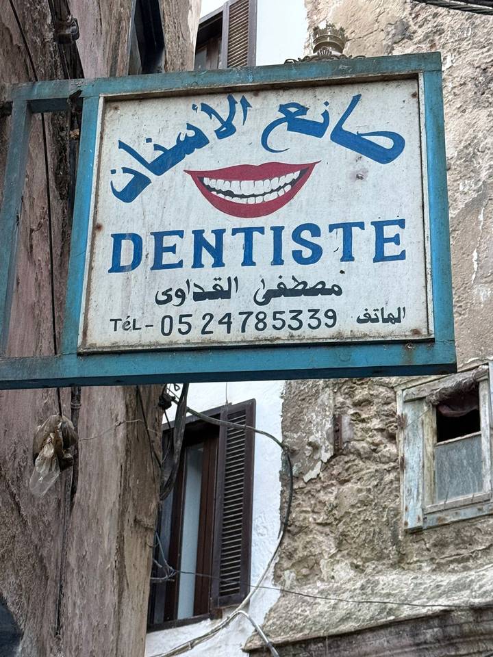 Weathered French-Arabic dentist sign hangs on an old medina wall.