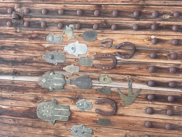 Weathered wooden door adorned with metal hamsa hand amulets, horseshoes and other talismans.