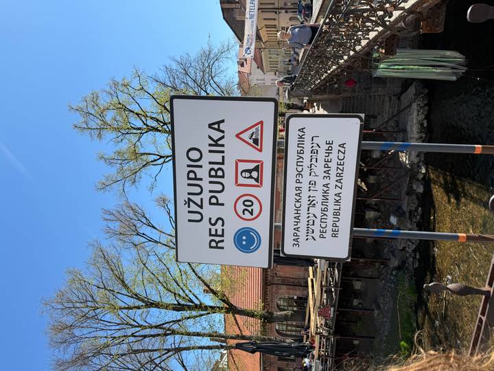 Bilingual sign announcing the Republic of Užupis art district beside a small canal.