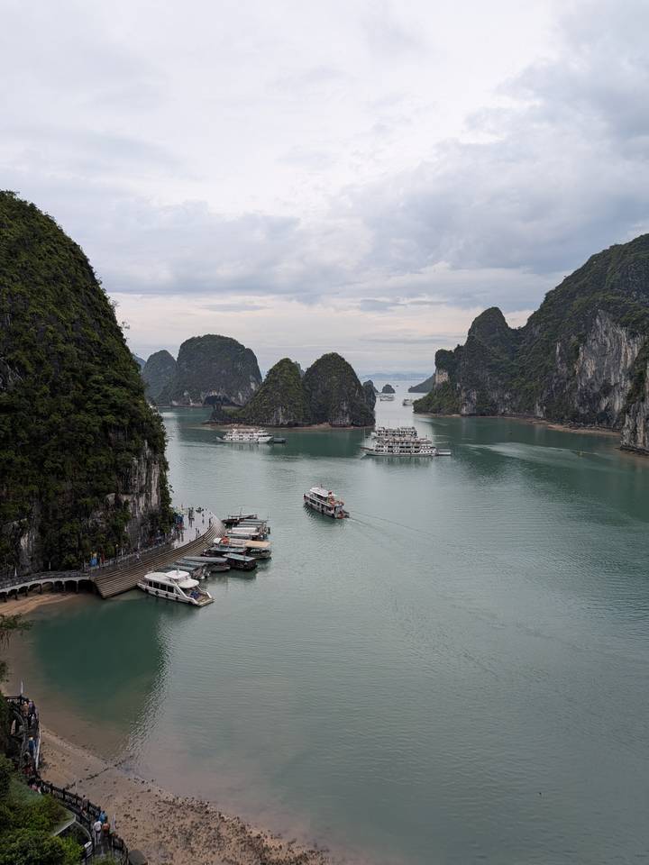 Panoramic overlook of Ha Long Bay with cruise boats weaving among dramatic limestone islands.