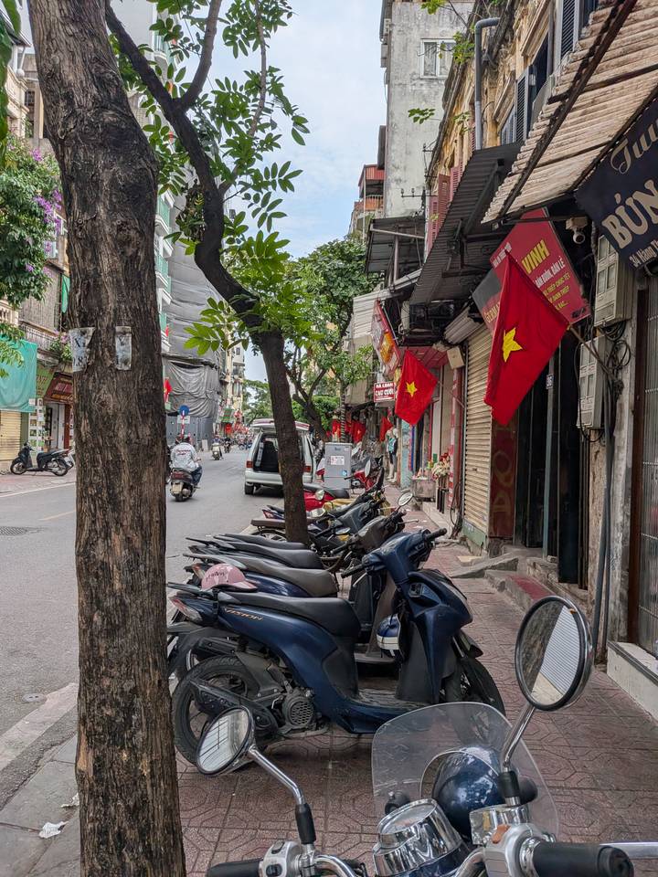 Narrow old-town Hanoi street with motorbikes, shops and national flags.