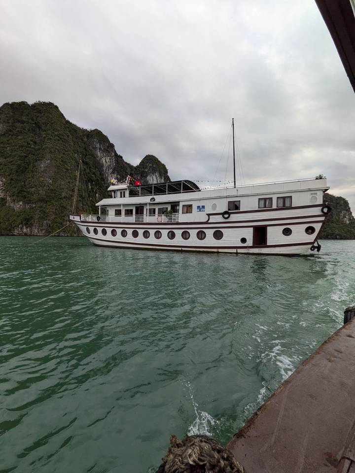White wooden cruise boat anchored in emerald waters of Ha Long Bay with towering karsts.