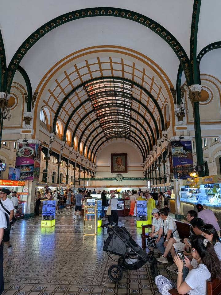 Interior of Ho Chi Minh City's Central Post Office with high arched ceiling and bustling visitors.