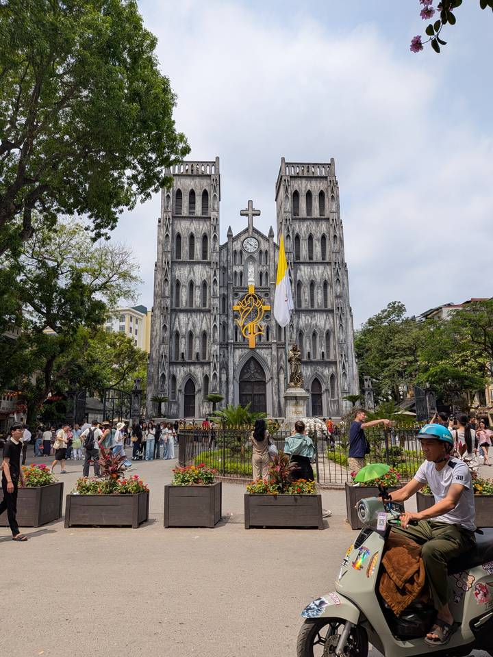 Gothic St. Joseph's Cathedral in Hanoi towers over bustling visitors and street vendors.