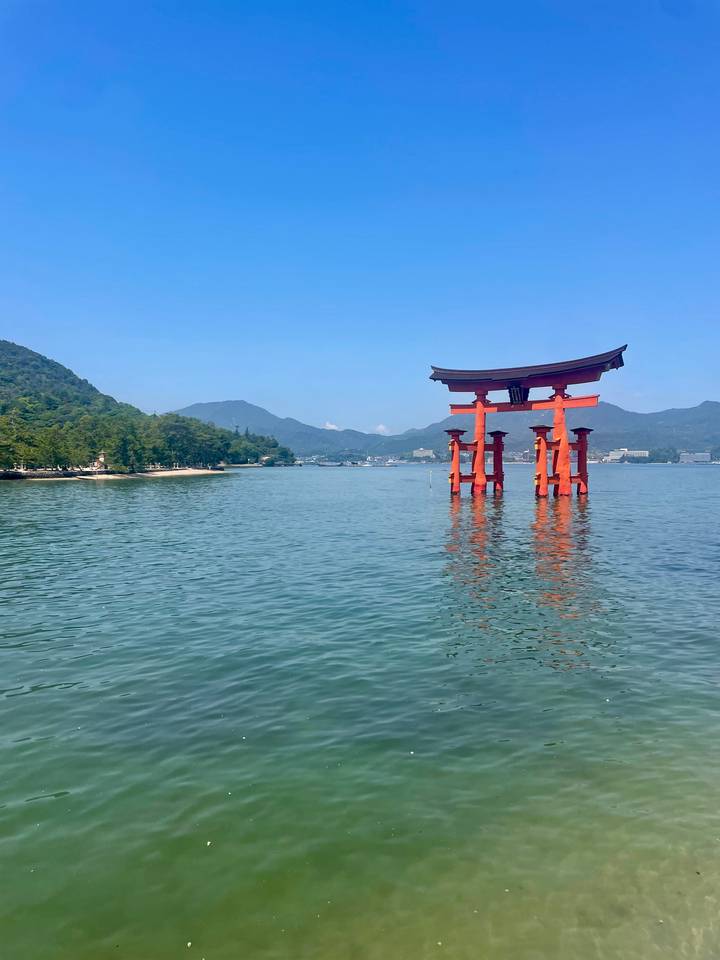 Iconic red torii gate of Itsukushima Shrine stands in calm blue water against forested mountains