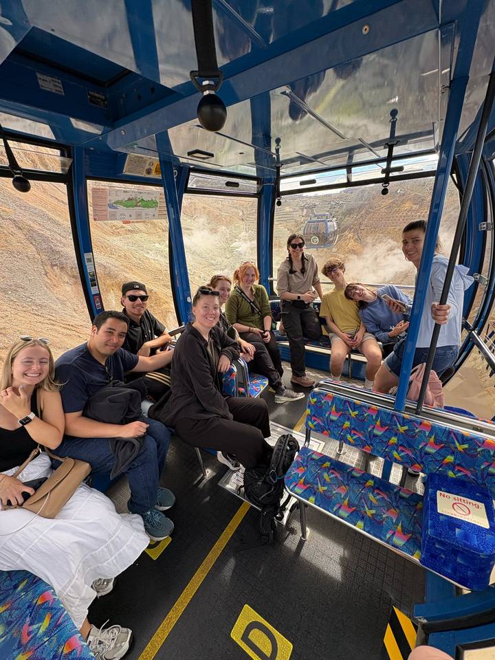 Smiling tour group seated inside a glass gondola overlooking volcanic terrain