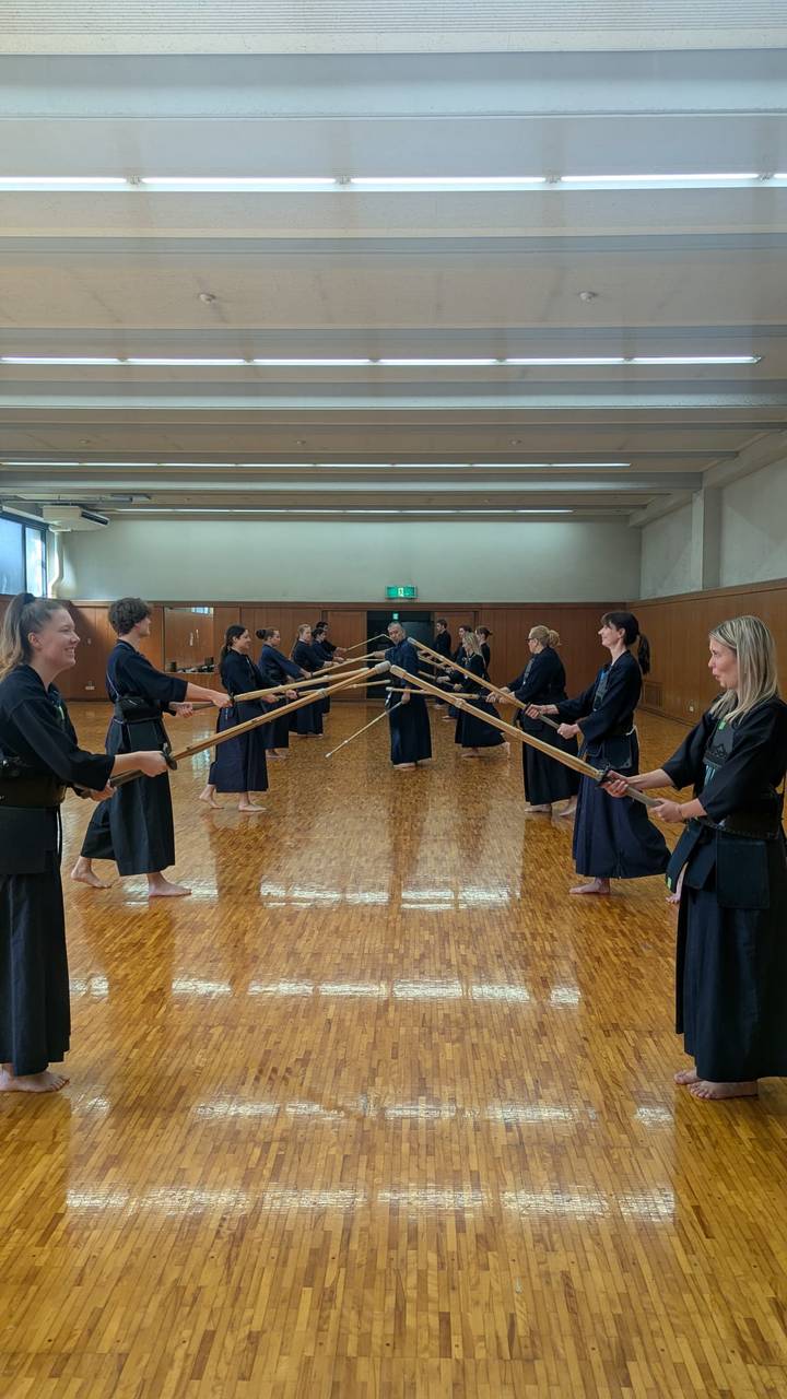 Participants in traditional kendo uniforms practice sword forms in a polished wooden hall