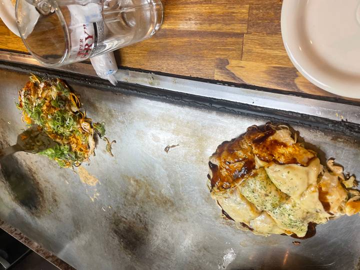 Freshly cooked okonomiyaki and toppings sizzle on a hot iron griddle in a restaurant