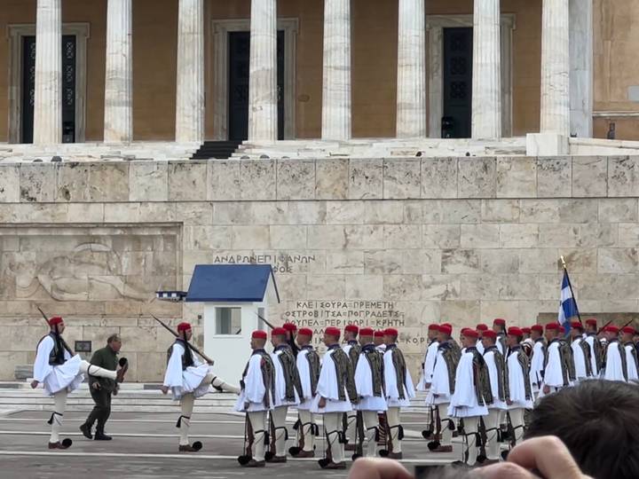 Evzone guards in traditional white uniforms and red caps march in formation during the changing of the guard ceremony.