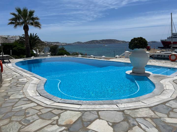 A turquoise hotel infinity pool overlooks the Aegean Sea and distant rocky islets on a bright day.