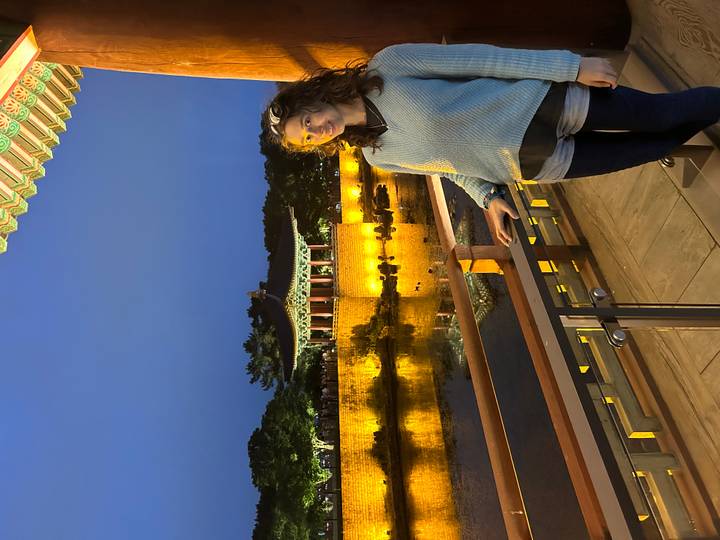 Visitor posing on a balcony beside the illuminated pavilion and moat of Gyeongju’s Donggung Palace at dusk.