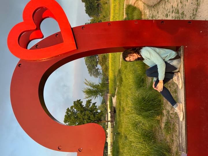 Traveller sitting inside a giant red heart sculpture in a grassy park at sunset.
