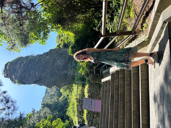 Traveller standing on stone steps beneath a towering volcanic rock spire in lush forest.