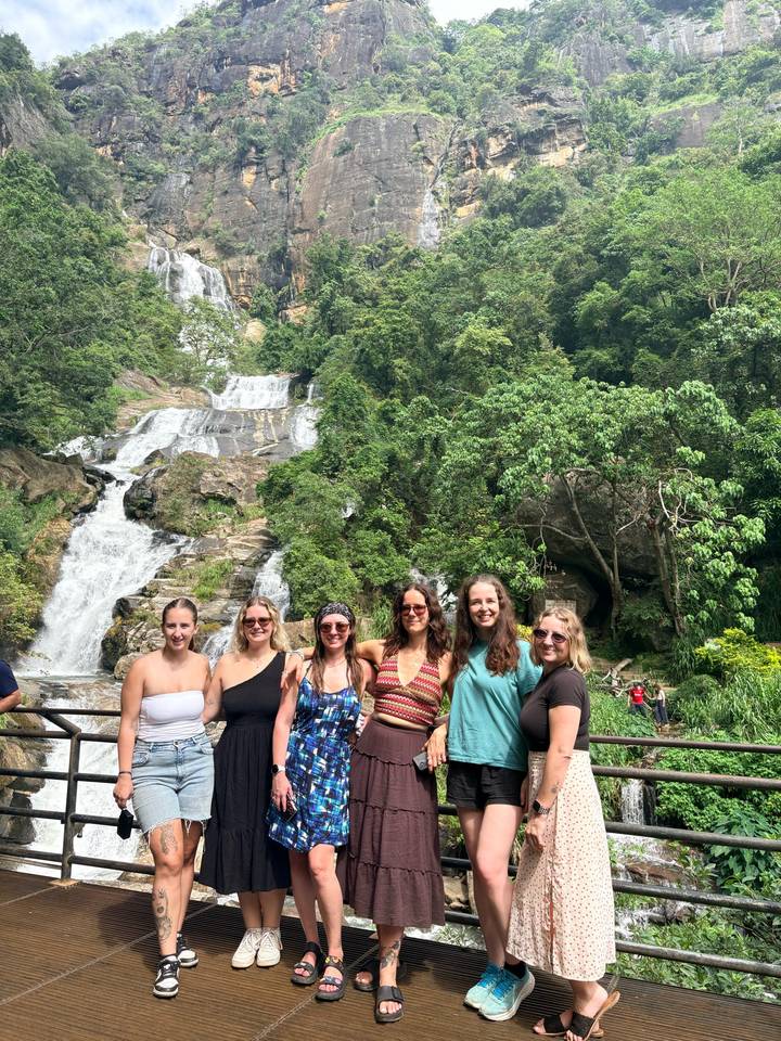 A group of travellers gather in front of a multi-tiered jungle waterfall.