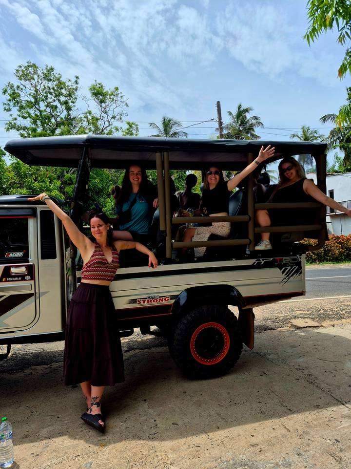Travellers cheerfully pose in an open safari truck on a rural roadside.