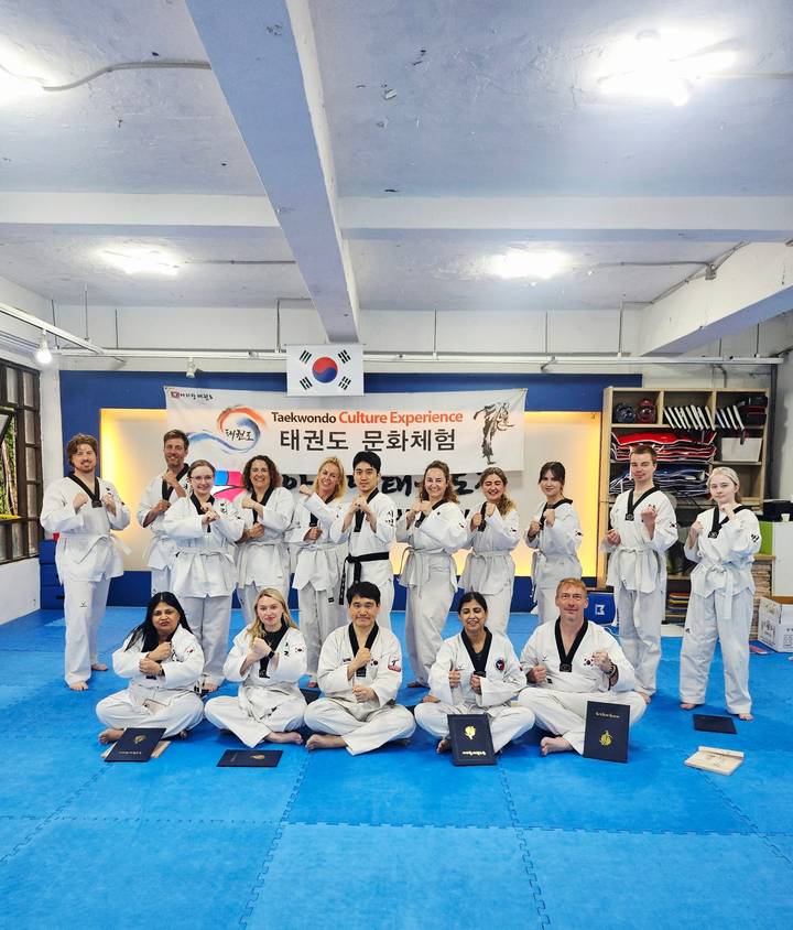 Group of taekwondo participants in white uniforms pose together in a martial arts studio.