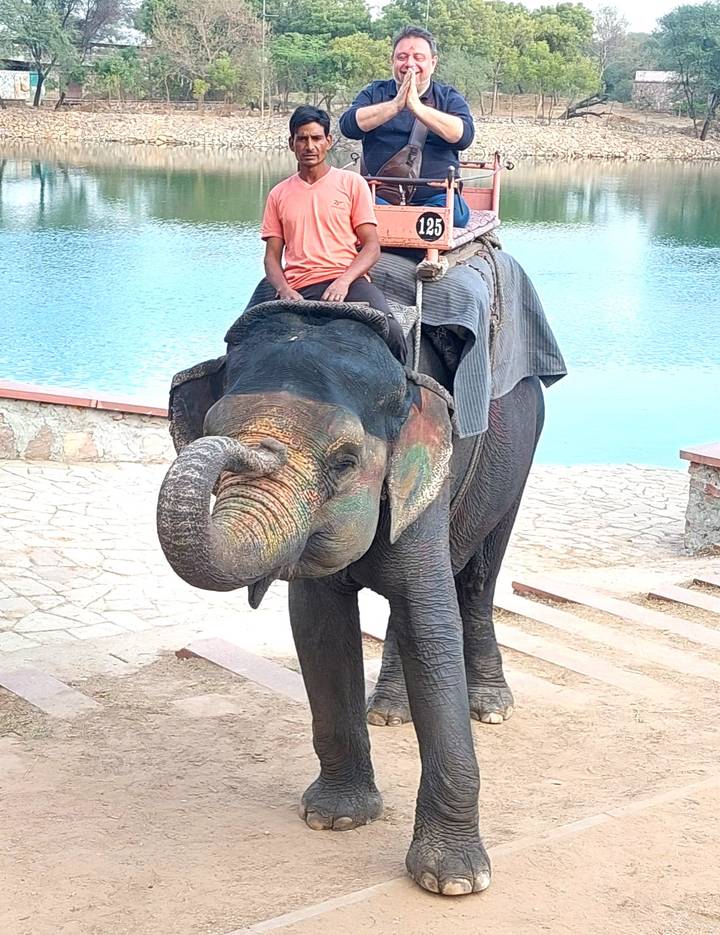Tourists riding a decorated Asian elephant by a lake on stone steps.