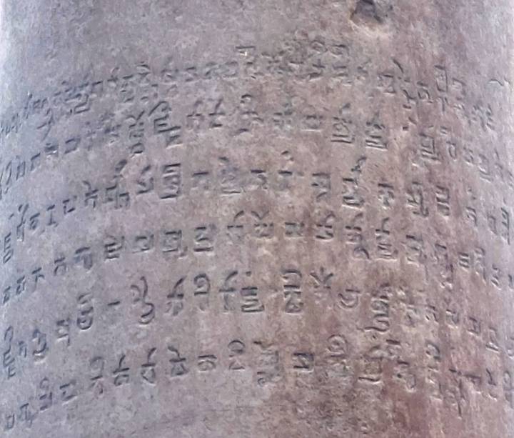 Weathered stone pillar carved with ancient Brahmi-like script, close detail shot.