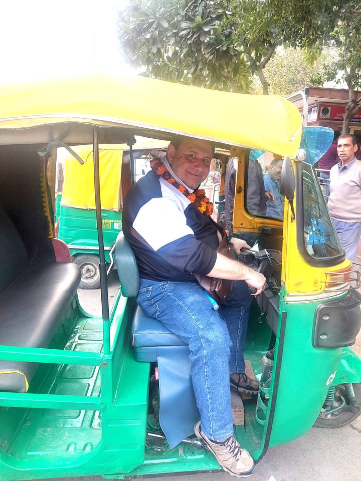 Smiling man seated in a colorful auto-rickshaw on a busy street