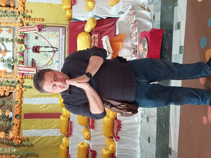 Man standing with hands in prayer inside a decorated temple hall with colorful fabrics
