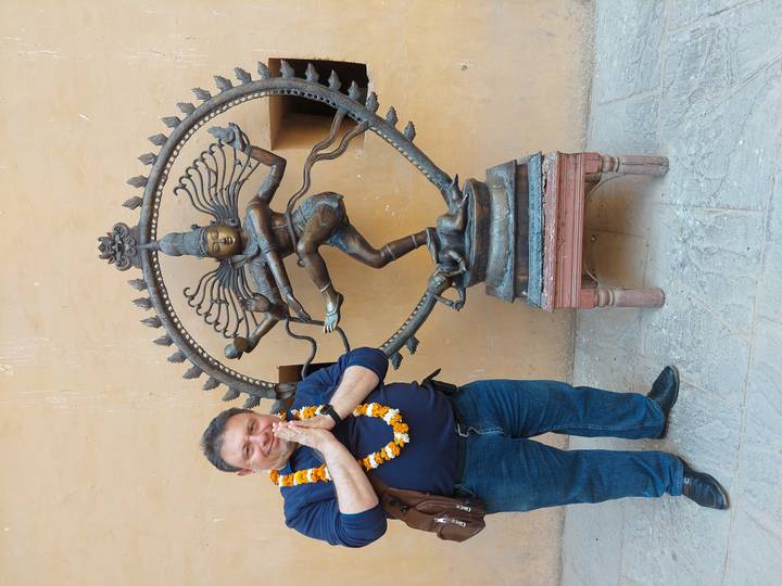 Man standing beside a bronze Nataraja statue with hands in prayer