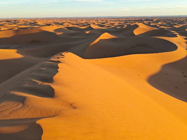 Vast orange sand dunes with dramatic shadows under late-day sunlight