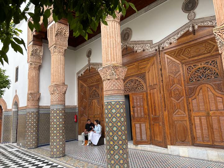 Visitors rest beside elaborately tiled columns and carved cedar doors in a Moroccan palace.