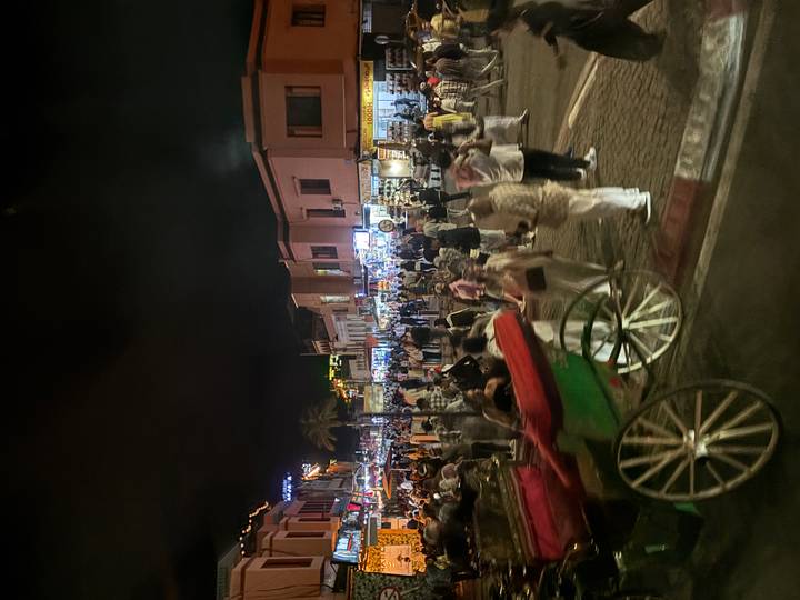 Night market in Marrakech teems with people, stalls and carriages under neon lights.