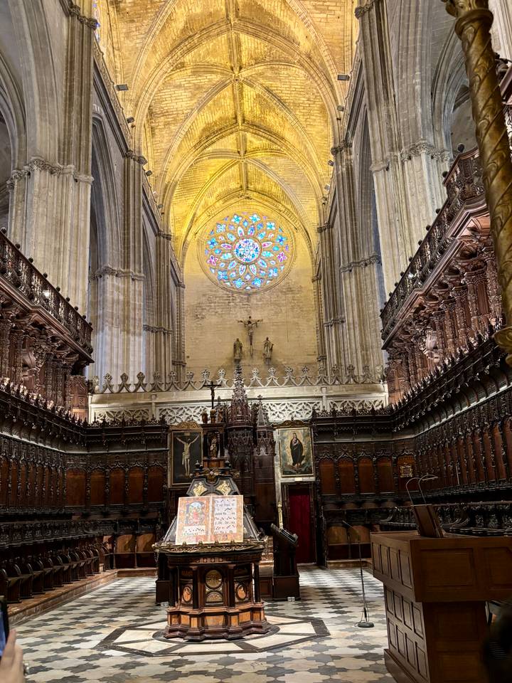 Interior of a grand gothic cathedral choir with soaring columns and a colorful rose window above the altar.