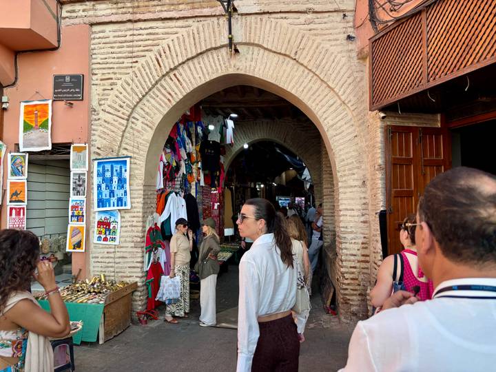 Tourists browse colorful stalls inside a brick archway market street.