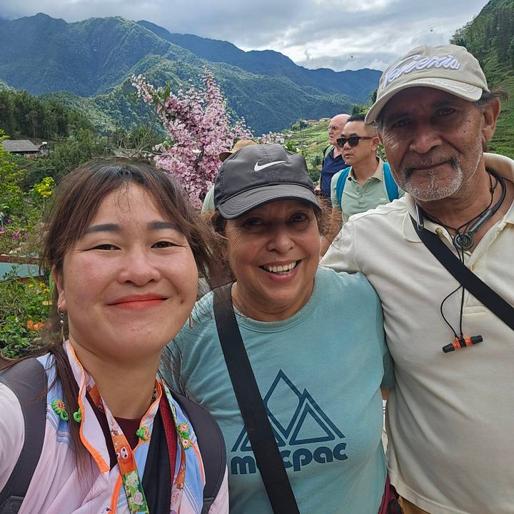 Smiling travelers and guide take a selfie with Sapa terraced hills and cherry blossoms behind.
