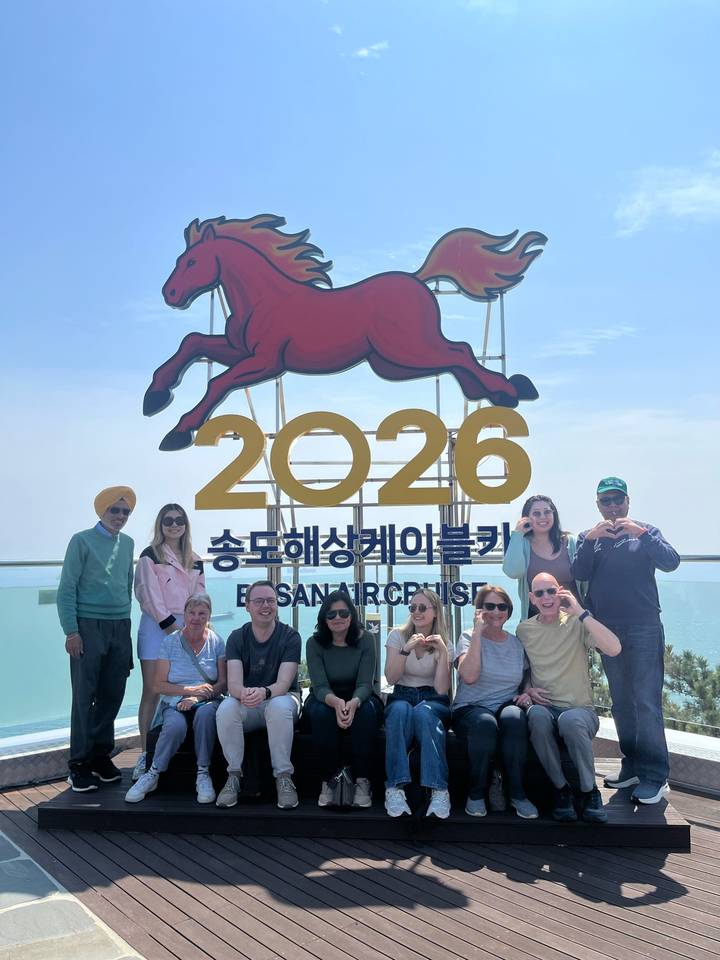Tour group poses under large red horse sign at Songdo Air Cruise lookout in Busan
