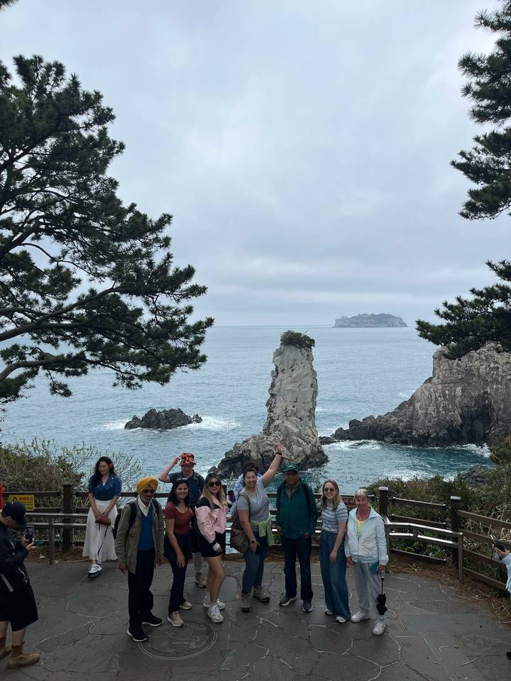 Travellers cheering on a cliffside path overlooking jagged sea stacks and grey ocean swell