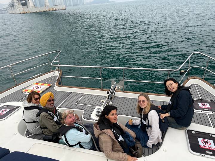 Small group relaxes on deck seats of a catamaran wearing life vests over calm harbour waters