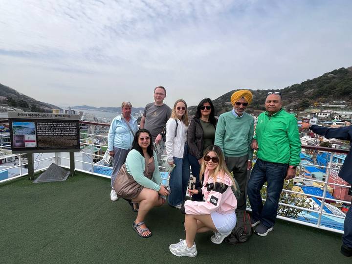 Travellers gather on a rooftop viewpoint overlooking colourful harbour town and surrounding hills