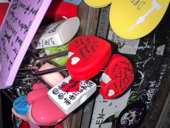 Close-up of colorful heart-shaped love locks covered in handwritten messages hanging on a rail.